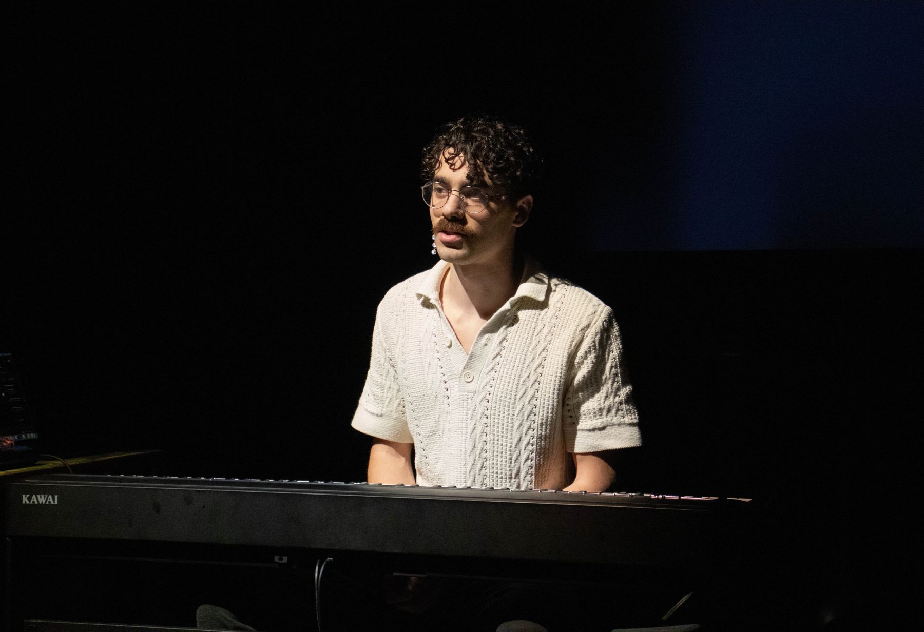 A performer at a keyboard in a single pool of light